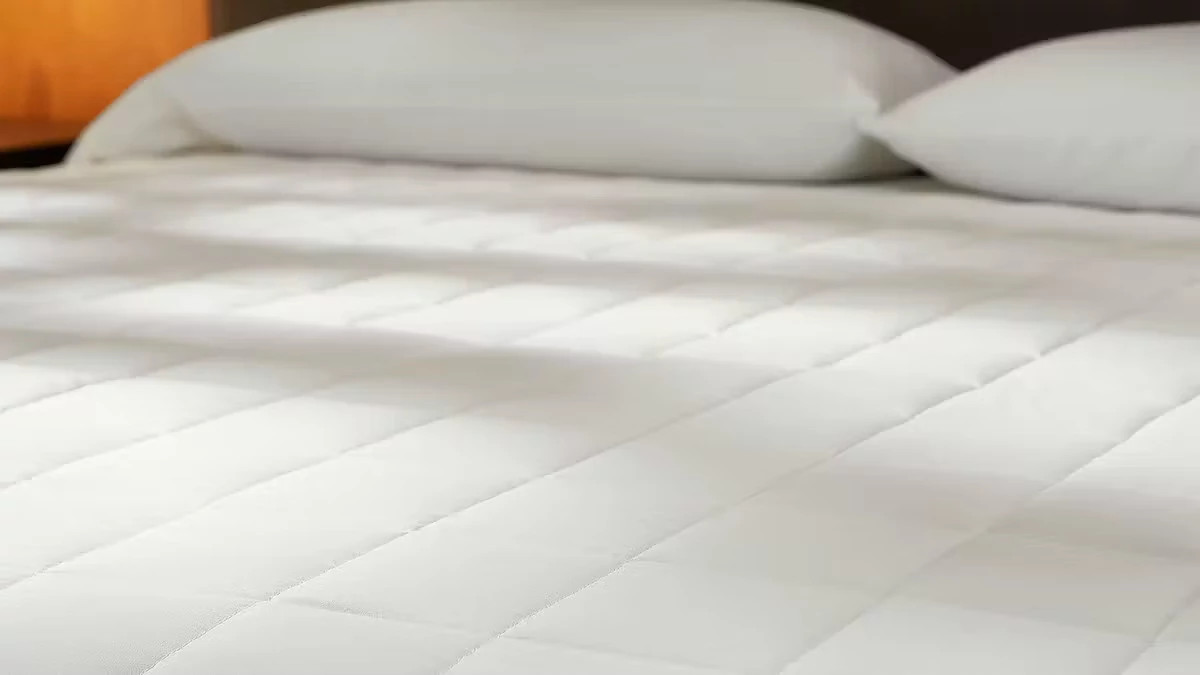 The Saatva Signature Mattress Pad on a bed with pillows