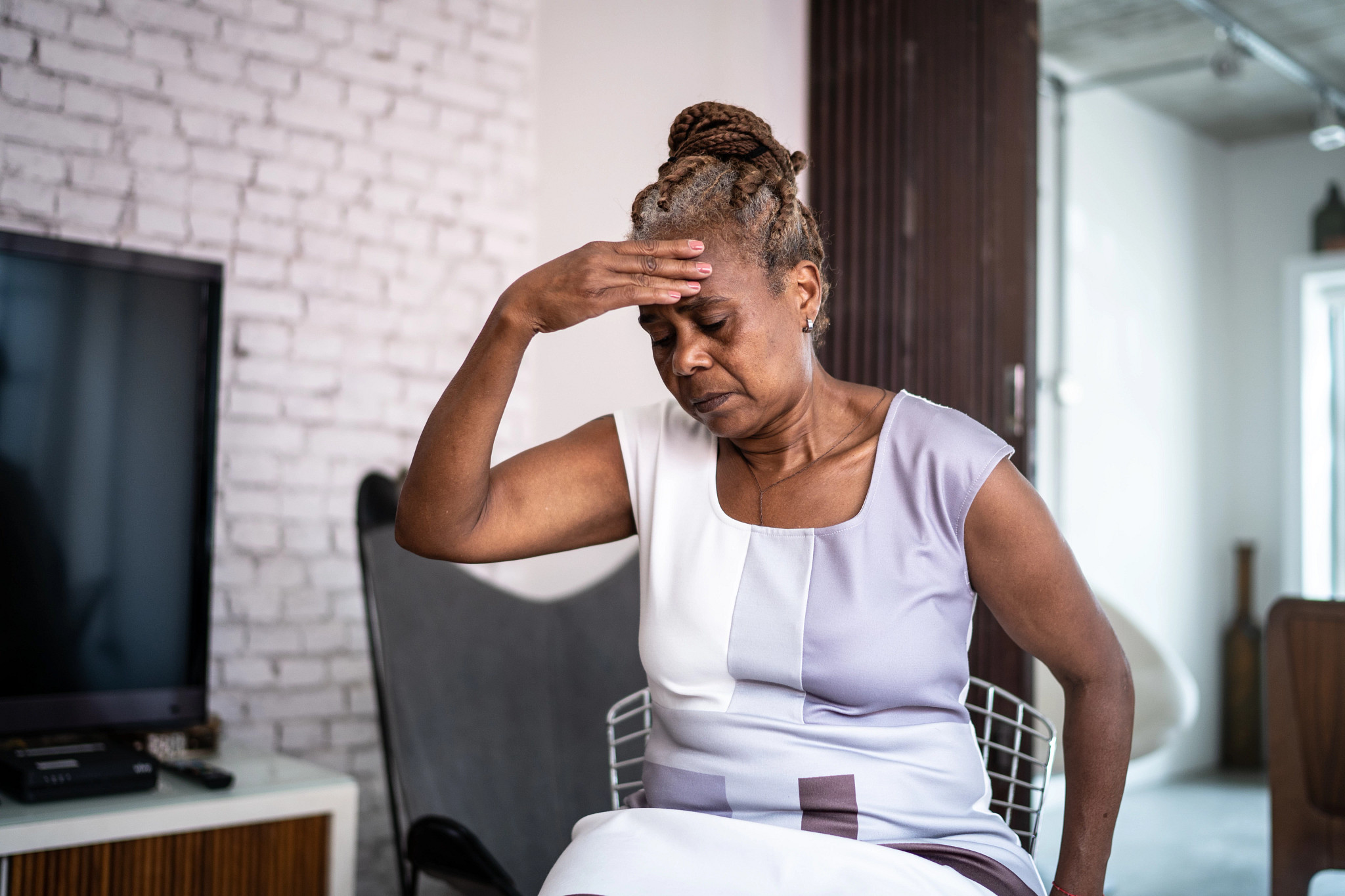 A woman with a headache sitting in a chair at home