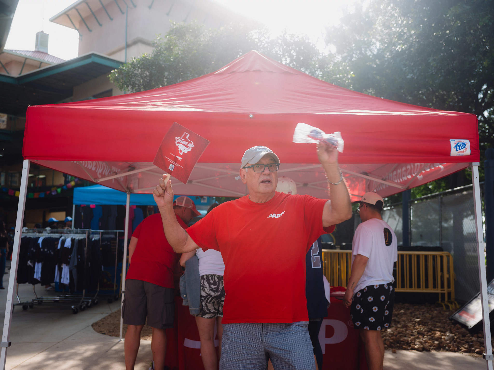 a man in a red AARP t-shirt in front of an outdoor booth
