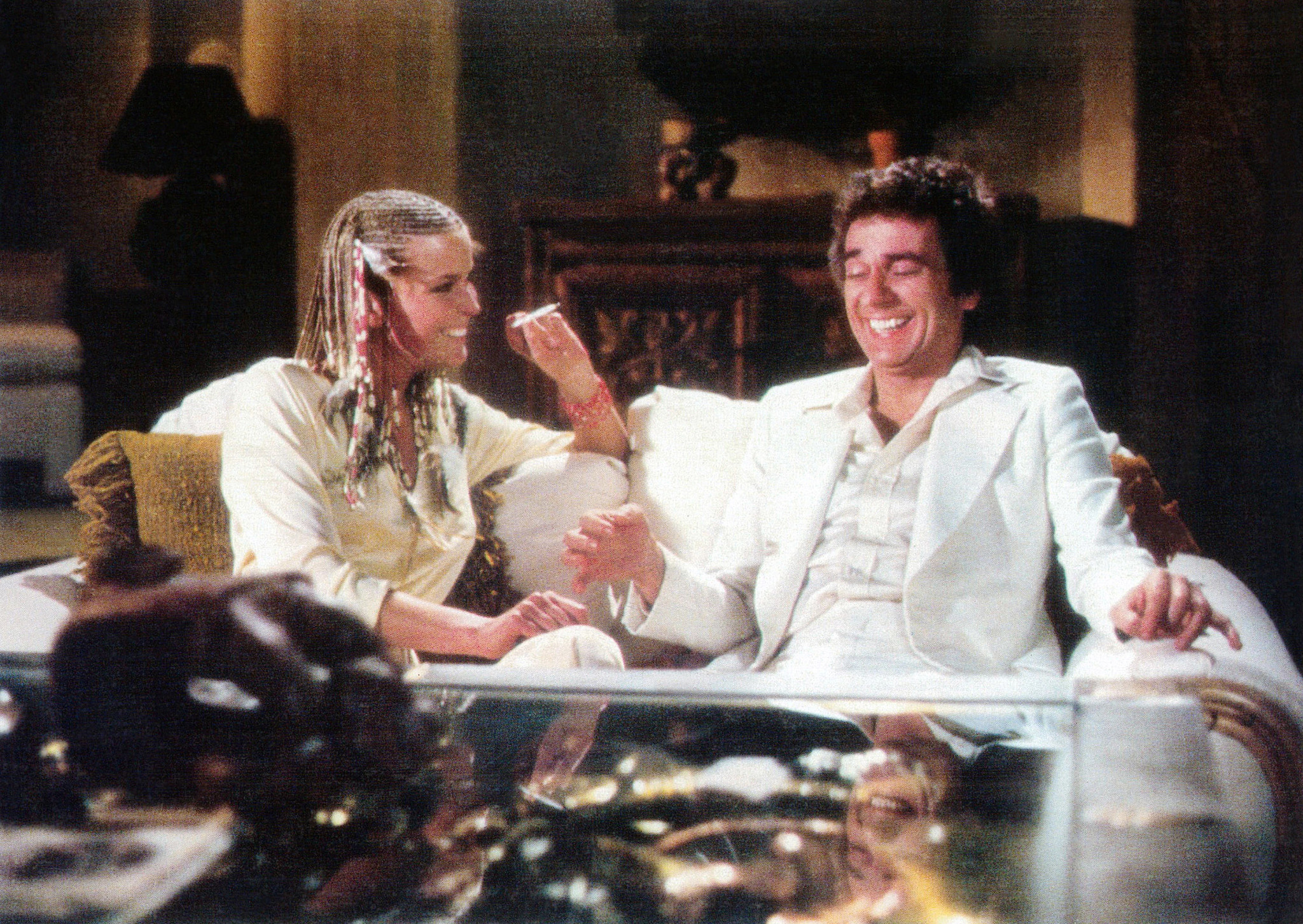 Bo Derek holding a cigarette sitting next to Dudley Moore on a couch in the film 10