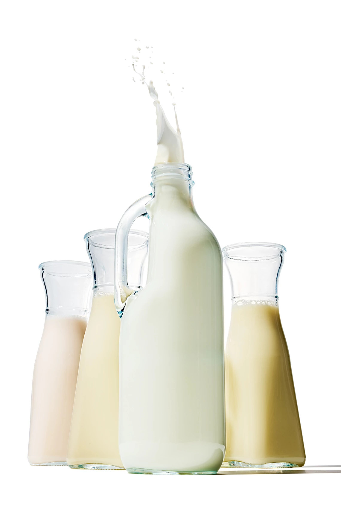 Four glass containers of milk, each a slightly different color of white