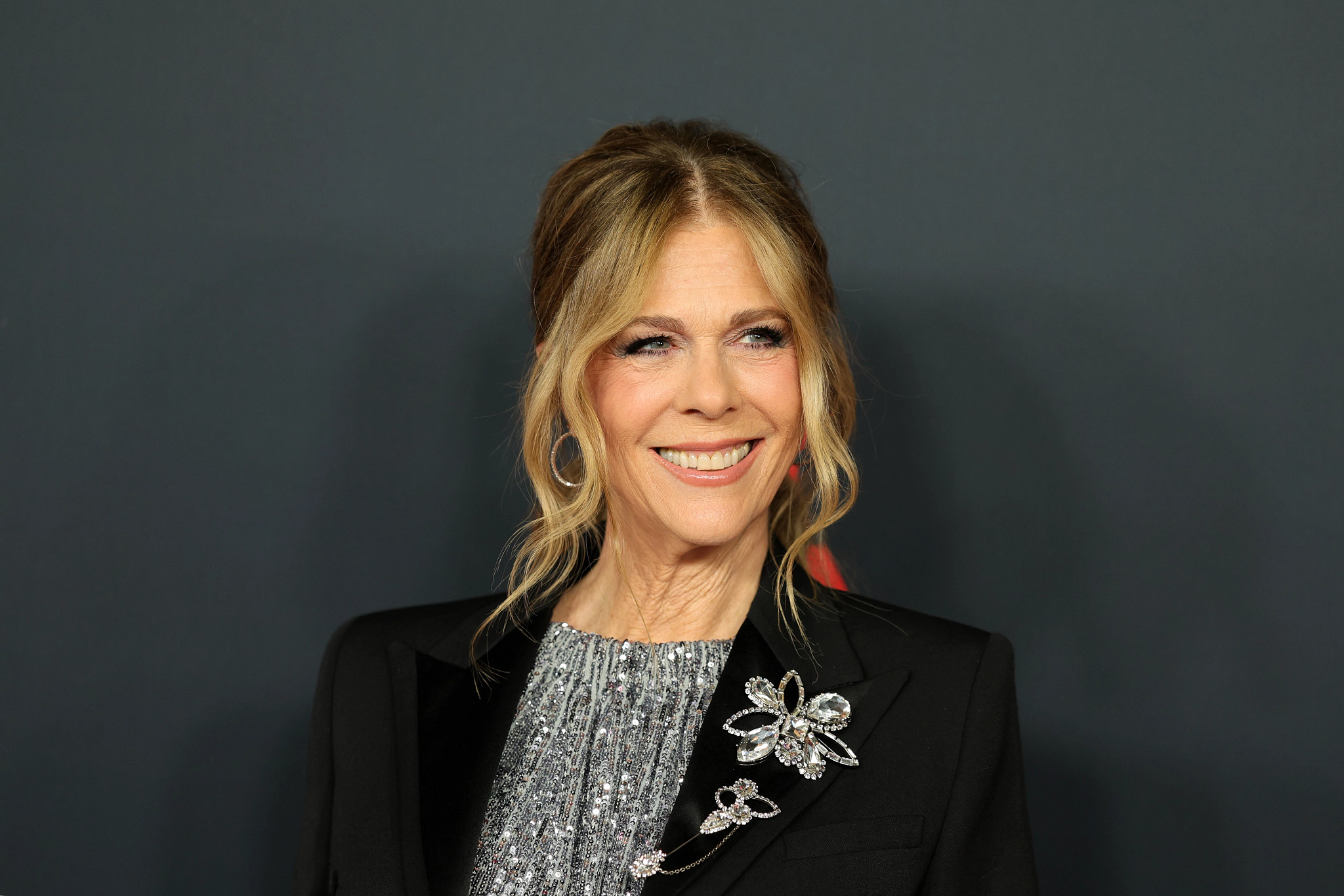 rita wilson smiling, wearing a black jacket and silver sequined top
