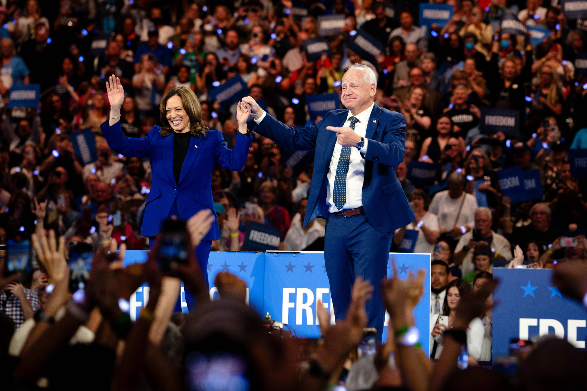 Kamala Harris saluda a la multitud mientras Tim Walz la señala.