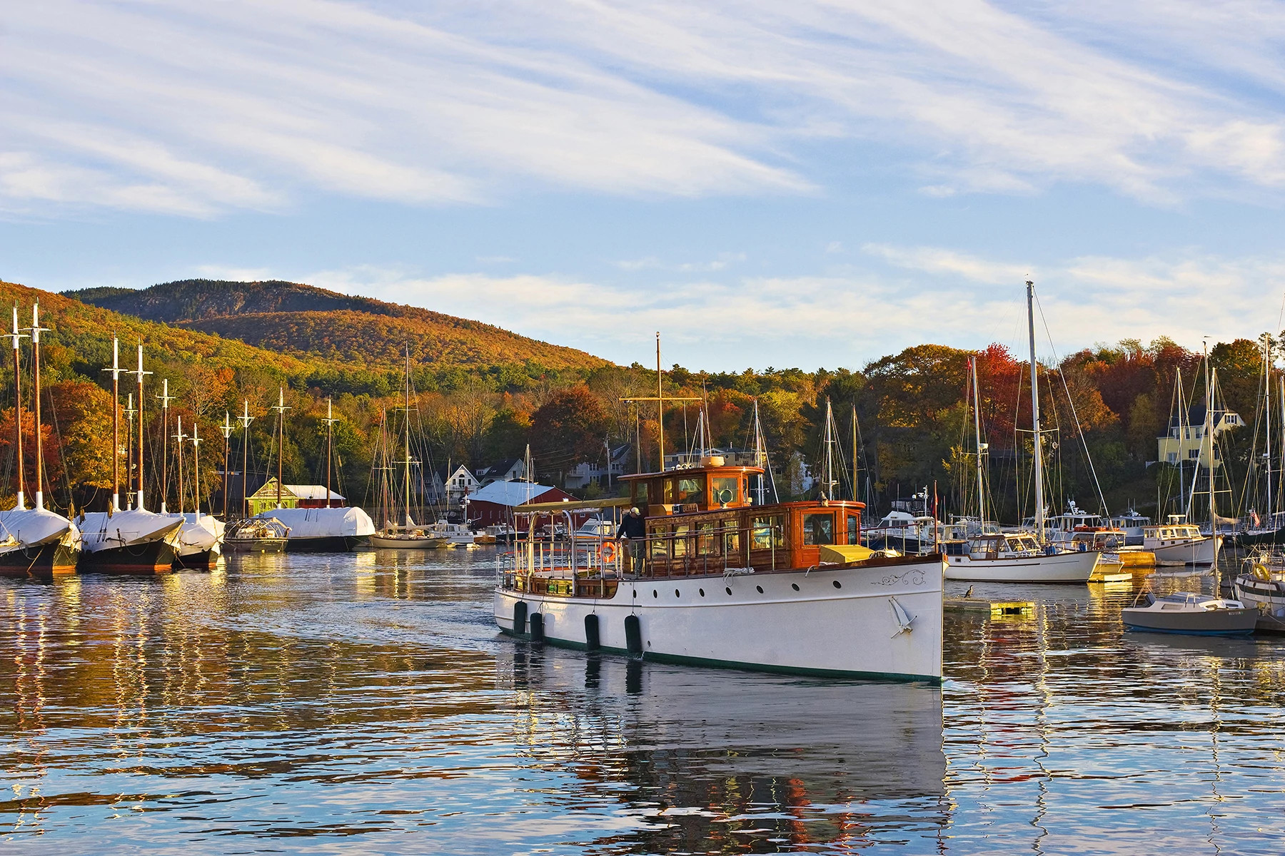 Classic wooden boat anchored in a harbor with autumn foliage and sailboats in the background