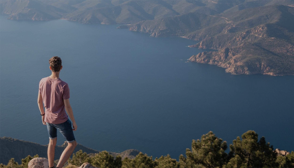 The Brain Health Atlas helps with health and economic burdens of brain disorders A man standing on the top of a peak looking out at the landscape and body of water