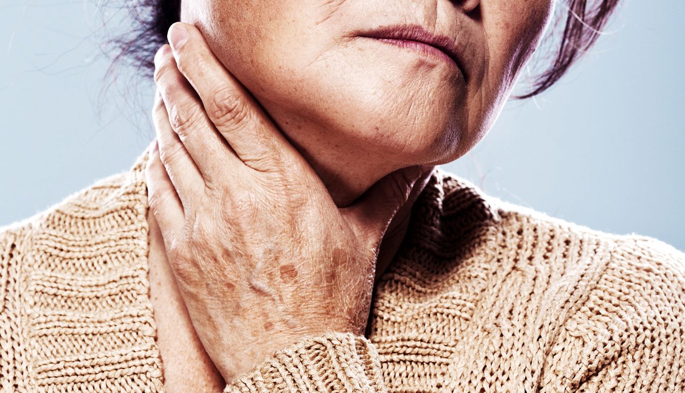 Una mujer se agarra la garganta con una mano