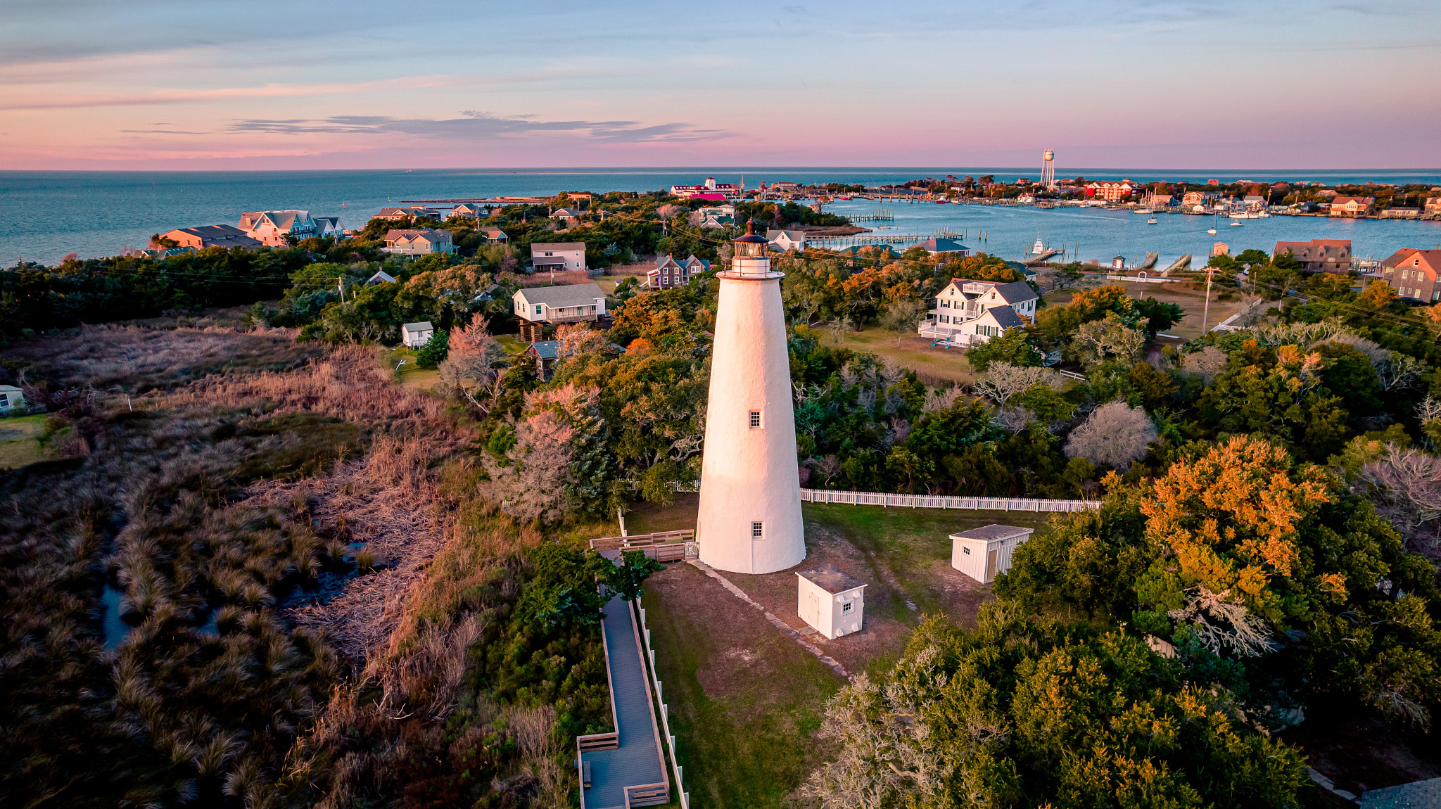 a lighthouse surronded by trees and houses near the water