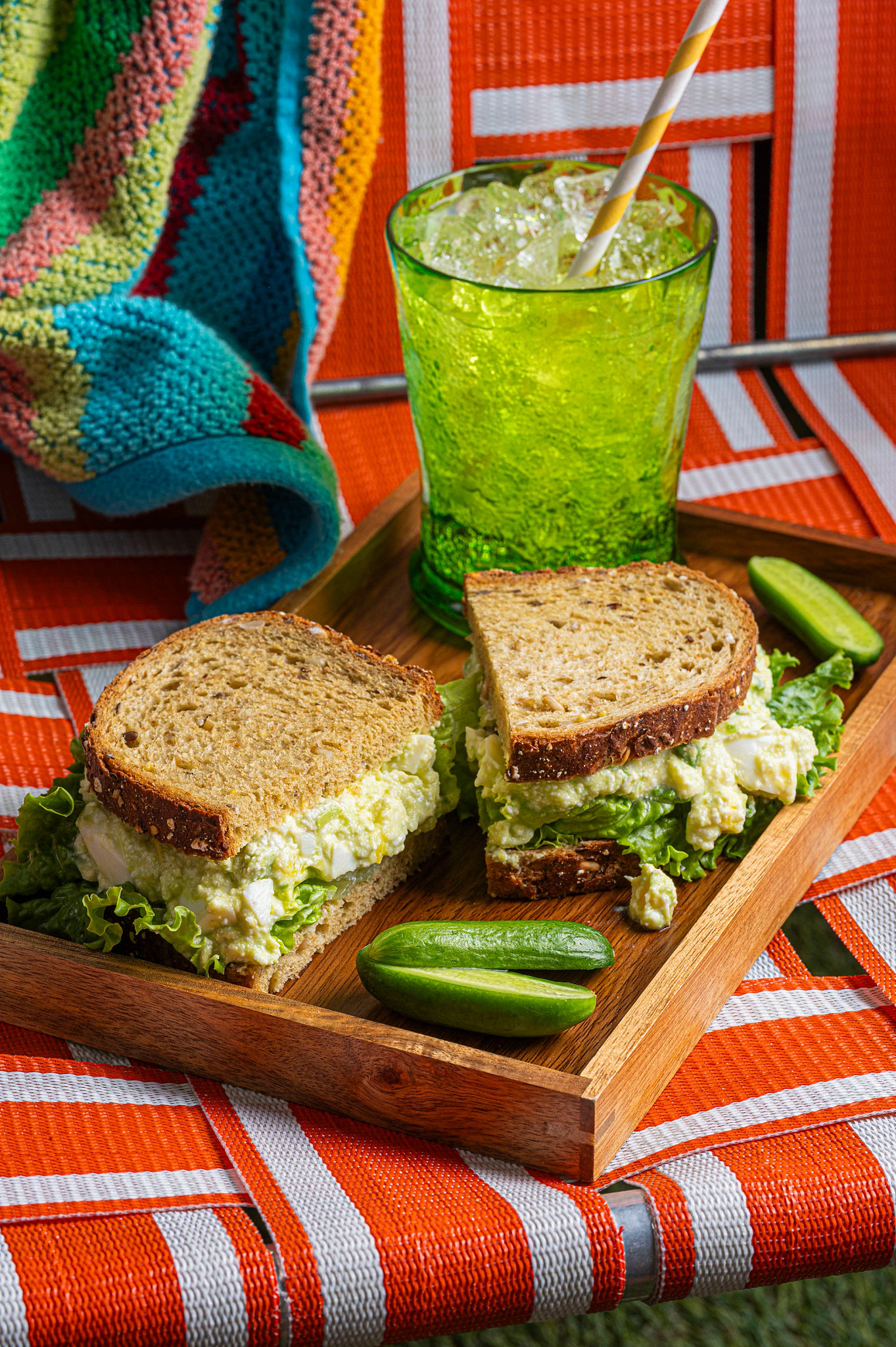 Healthy picnic lunch featuring egg salad with avocado and cottage cheese, fresh cucumber slices, and a sparkling drink in a green glass