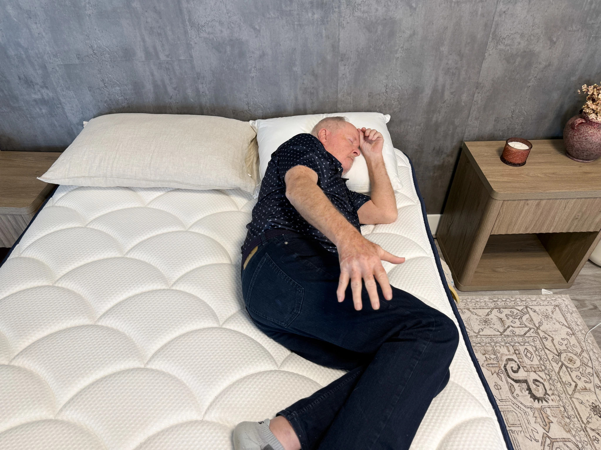 A man lying on his side on a mattress near a night stand