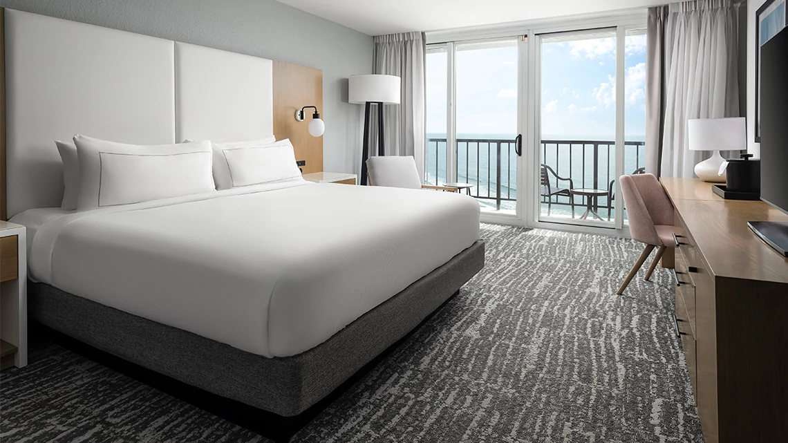 hotel suite with king size bed in white linens, balcony, ocean view