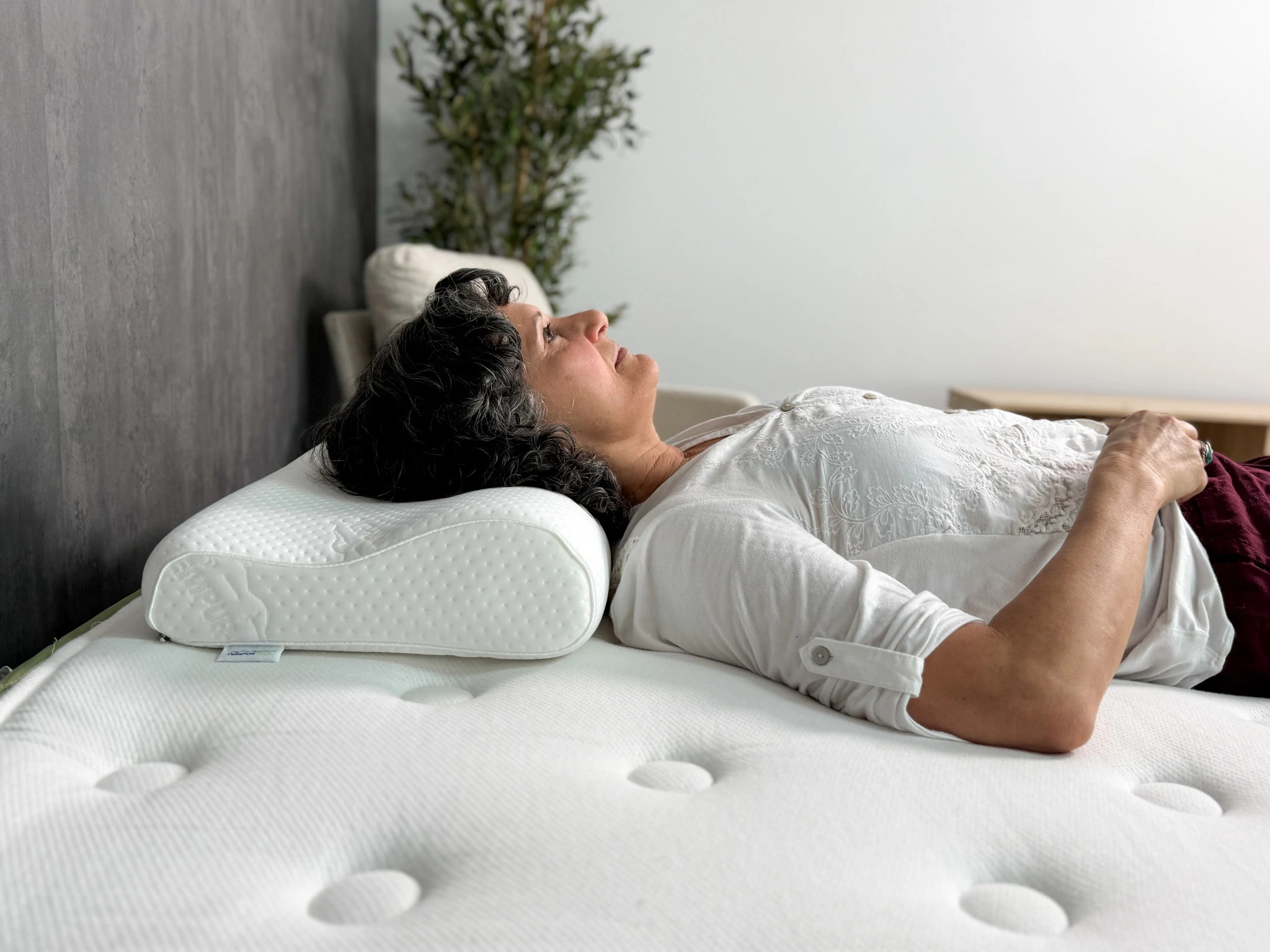 A woman lying on her back with her head resting on the Tempur-Pedic Tempur-Neck Pillow
