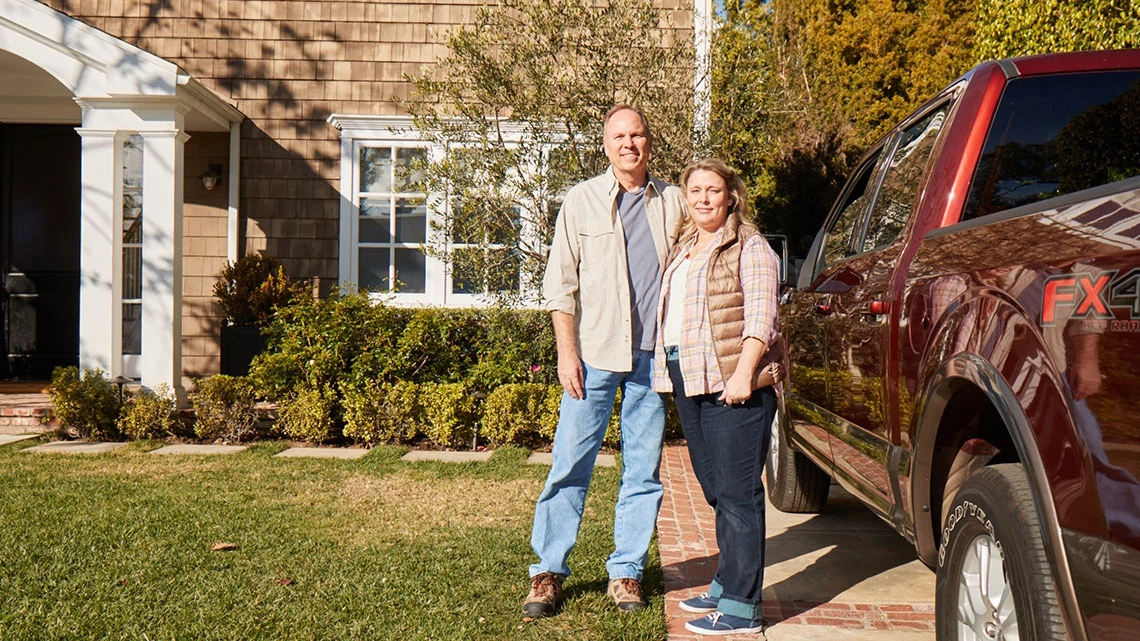 Couple standing next to each other, next to a truck outside home