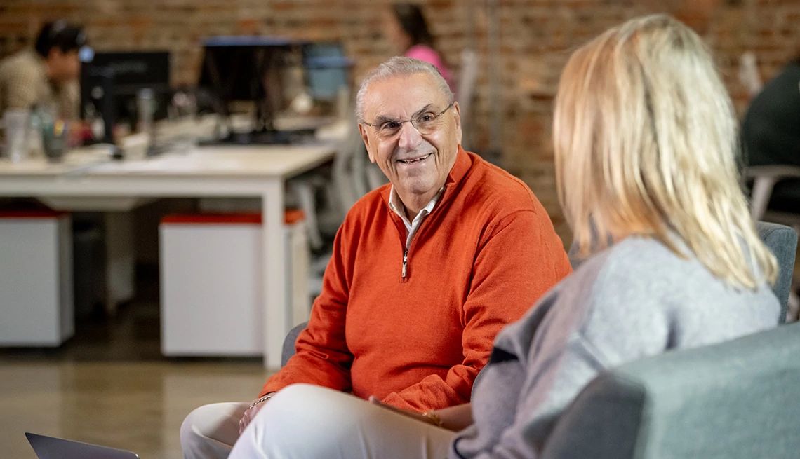 Los pasantes de oro de Naborforce forman parte de un programa de pasantías de retorno un hombre sonriendo sentado en una silla y con un suéter con cremallera