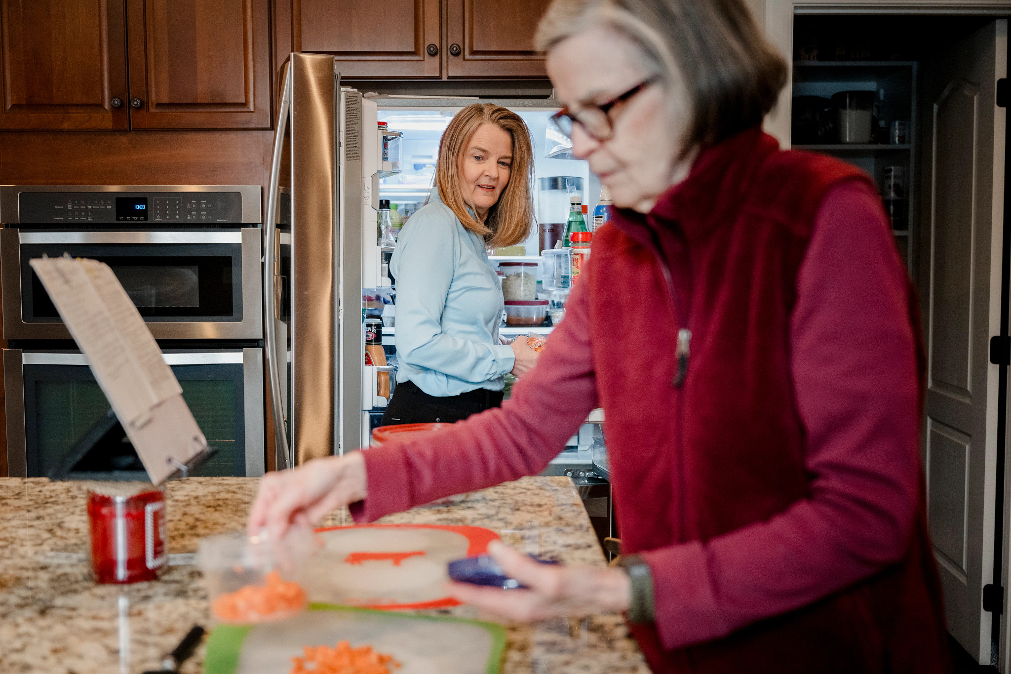 una mujer frente al refrigerador y otra preparando comida en la cocina.