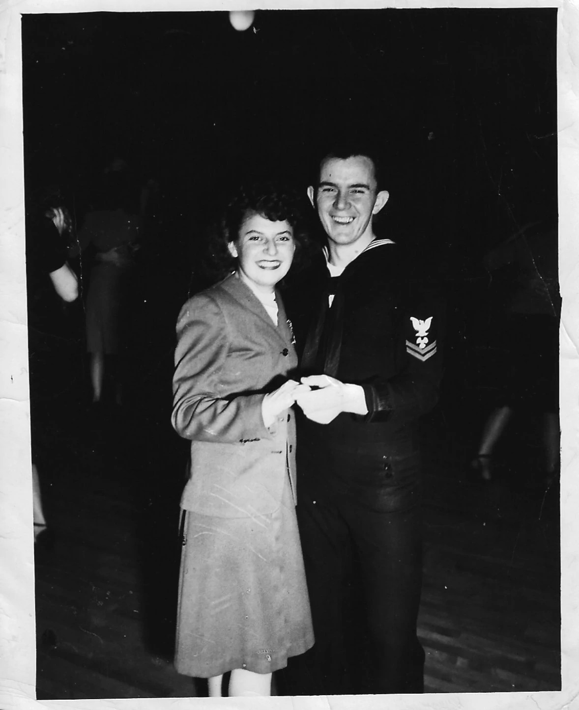 A man and woman smile and hold hands in a black and white photo.