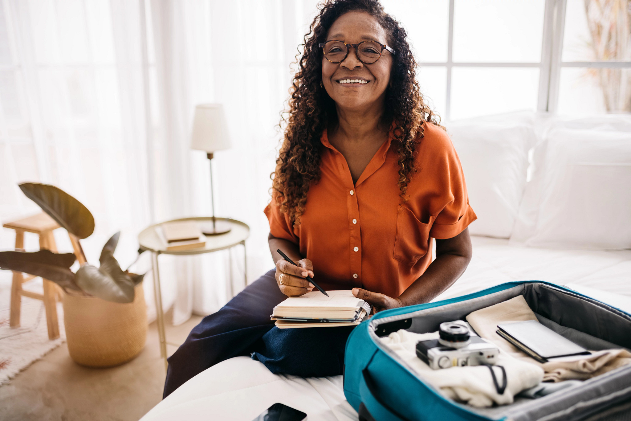 a woman sitting on a bed with a notebook and open suitcase next to her