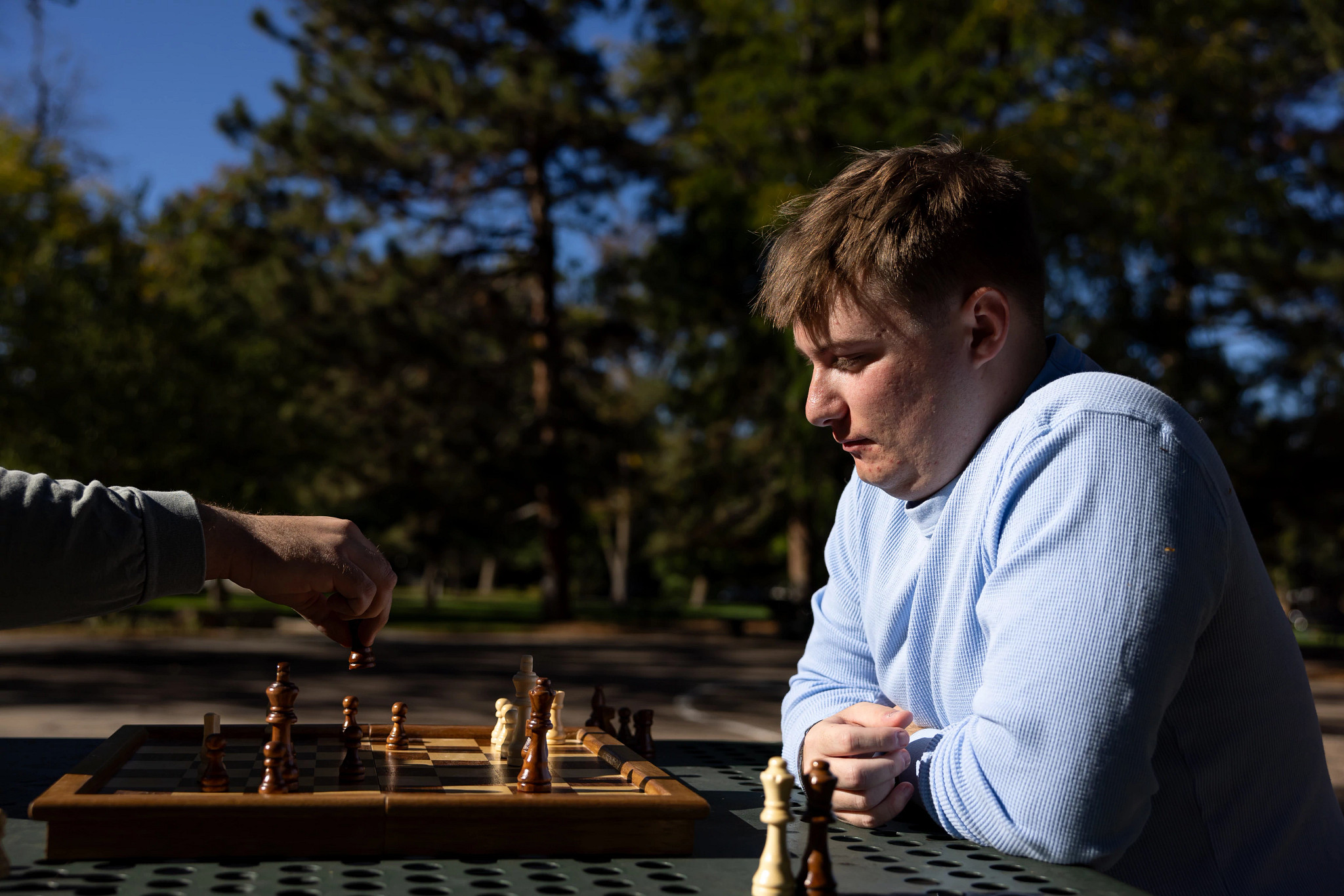 Evan Clark plays chess outdoors, watching his opponent make a move.