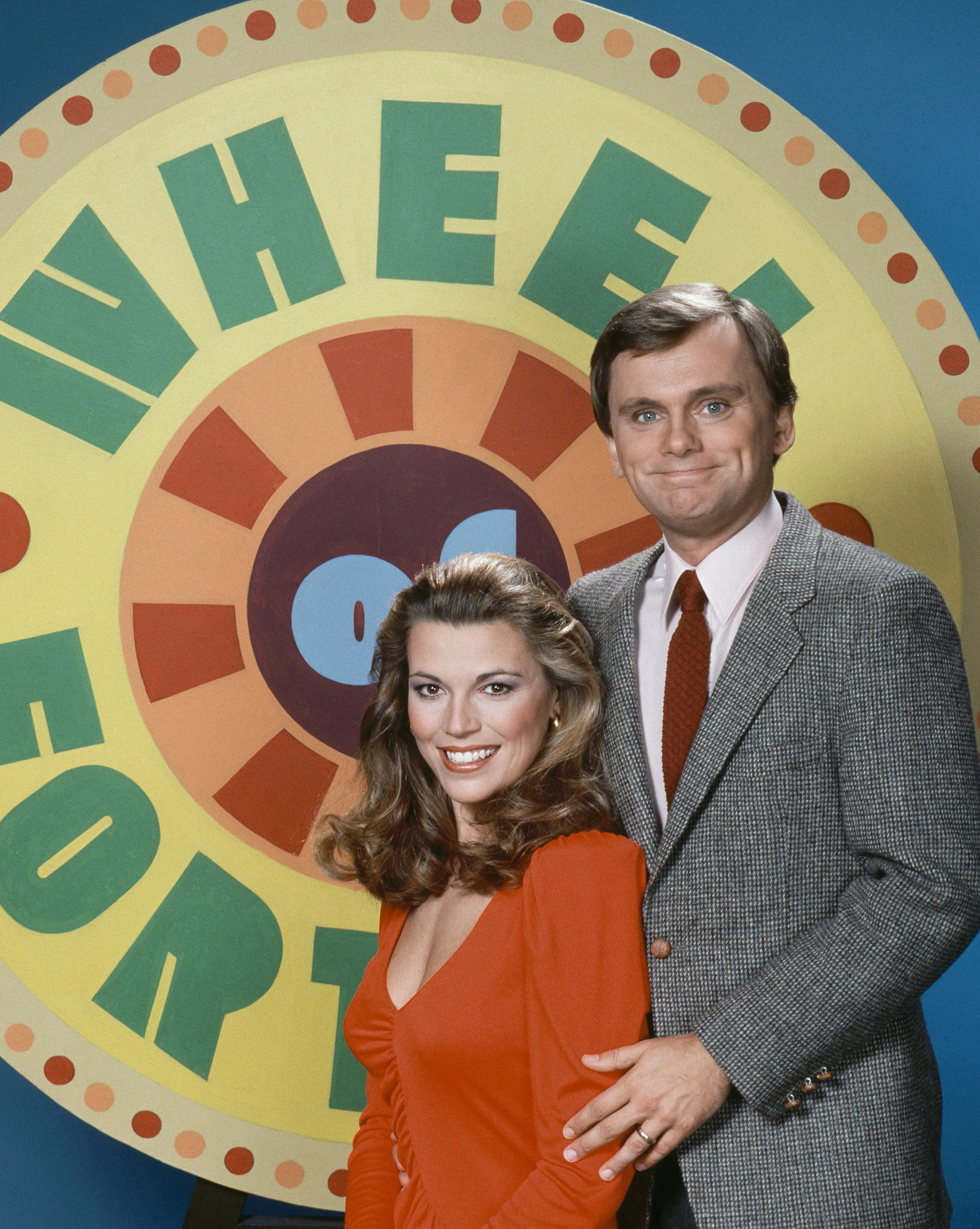 Vanna White and Pat Sajak in front of a logo for Wheel of Fortune