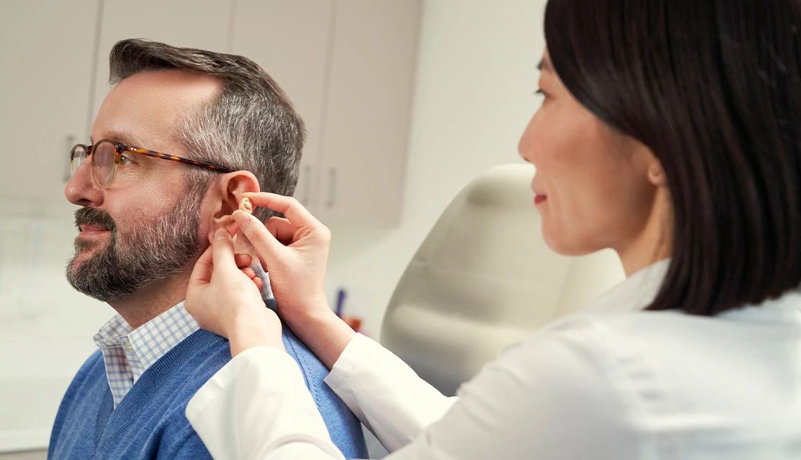 Doctor fitting hear aids for a man wearing glasses and a blue sweater