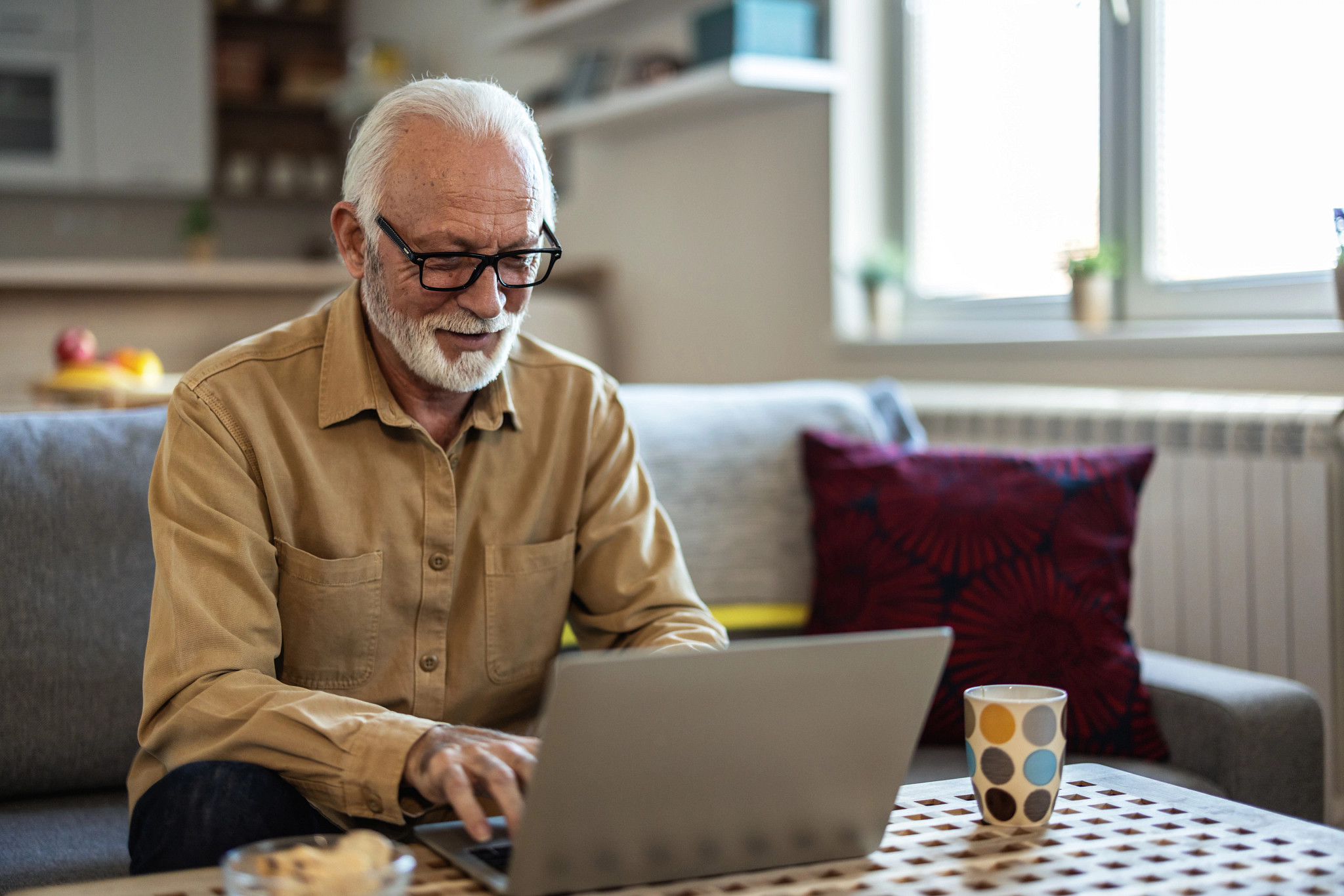 Smiling older adult man using laptop at home.