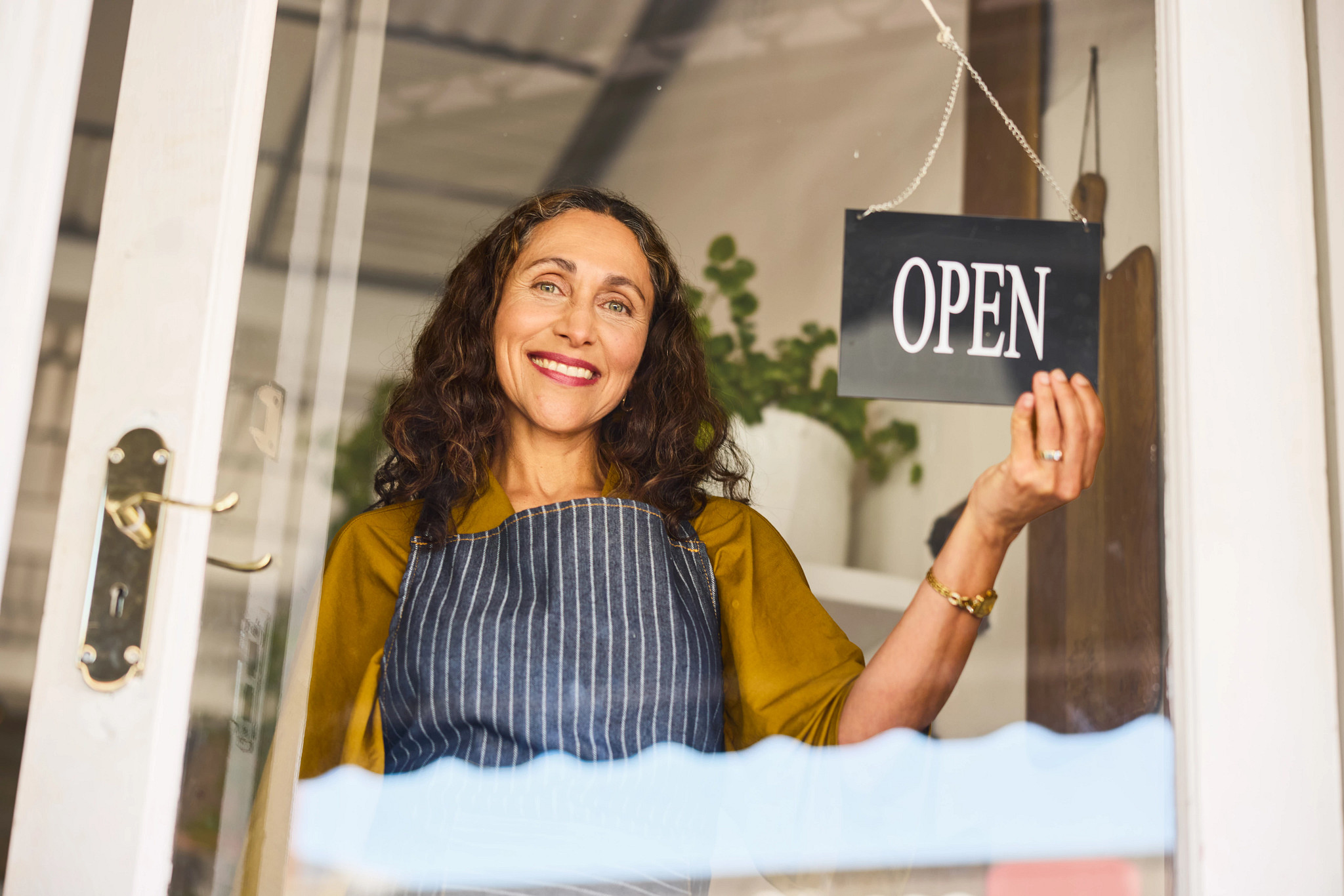 a woman smiling in a storefront while flipping a sign to open