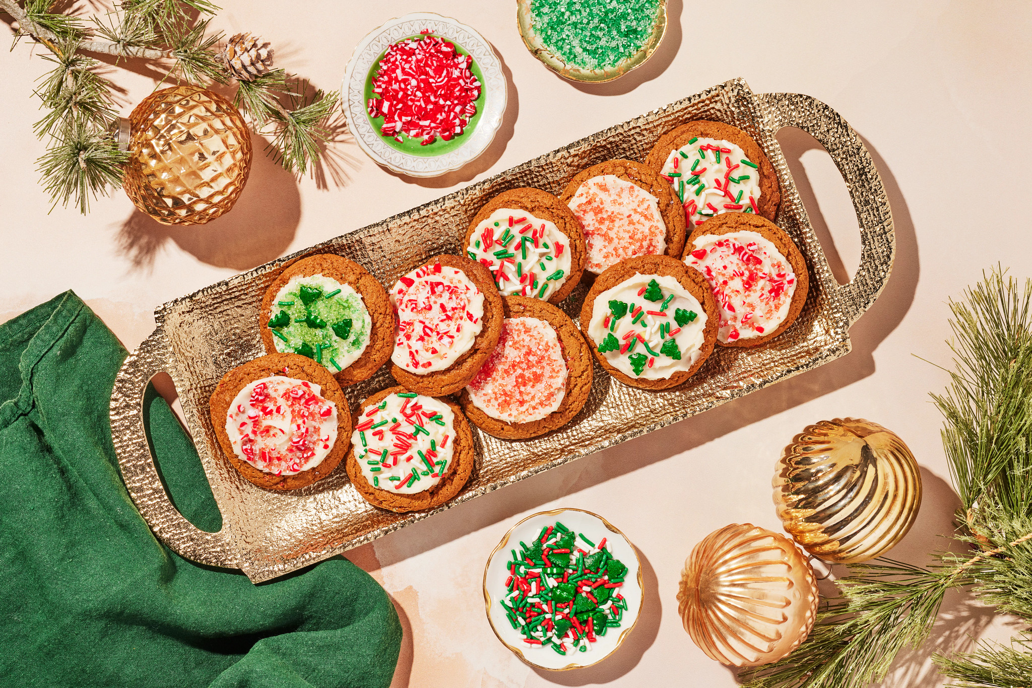 Frosted Christmas cookies with red and green sprinkles arranged on a woven tray surrounded by holiday ornaments
