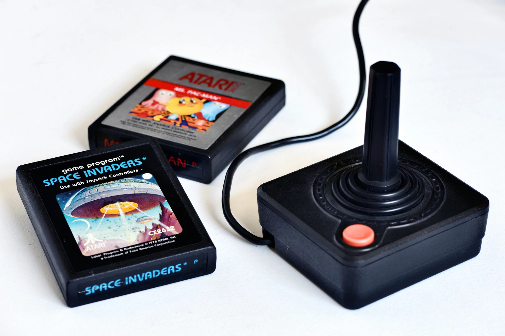a photo shows an Atari 2600 controller on a white surface, with space invaders and ms. Pac-man cartridges on the side