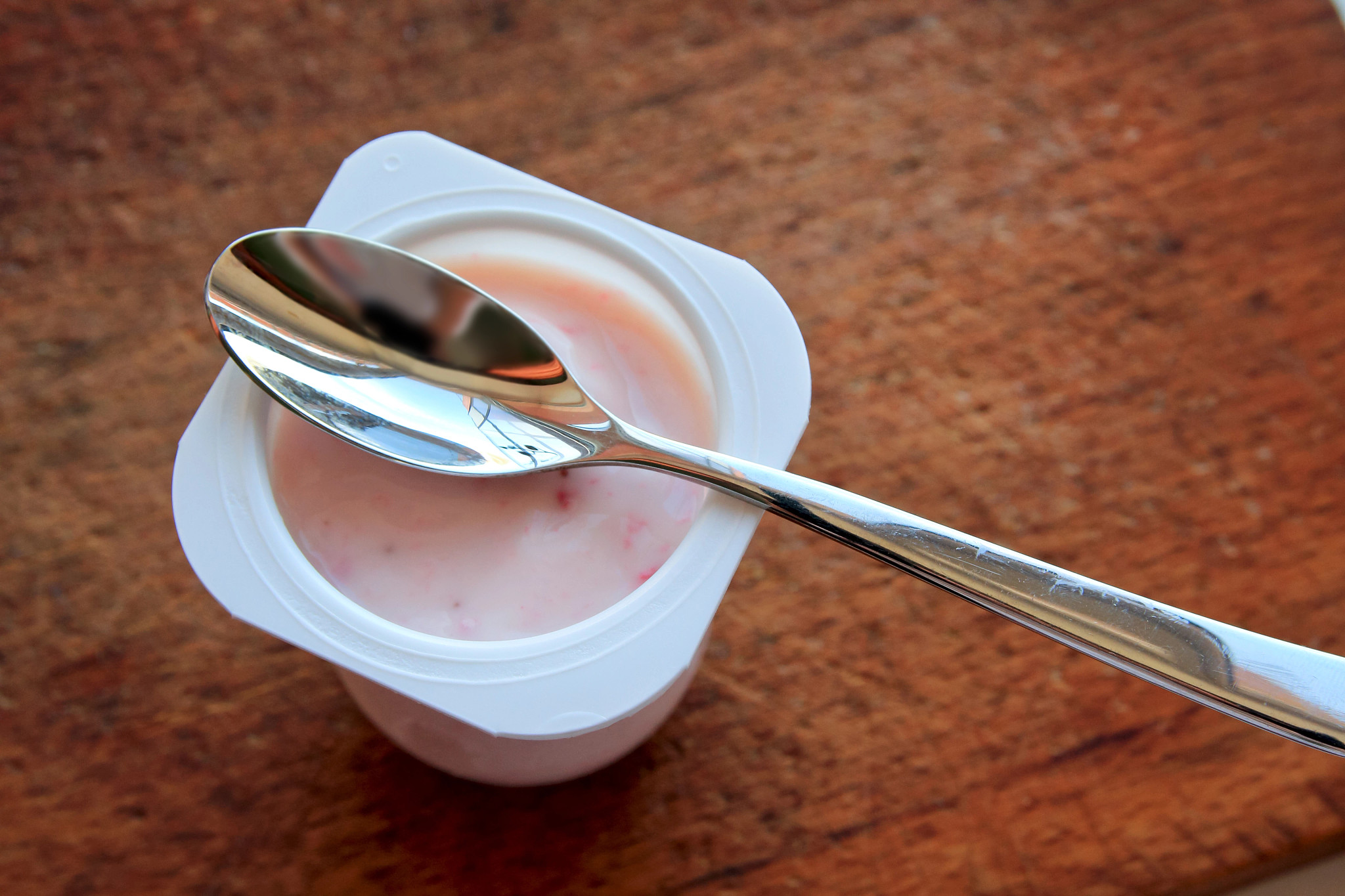 Strawberry pink yogurt in white plastic cup on a wooden rustic background with spoon on it.