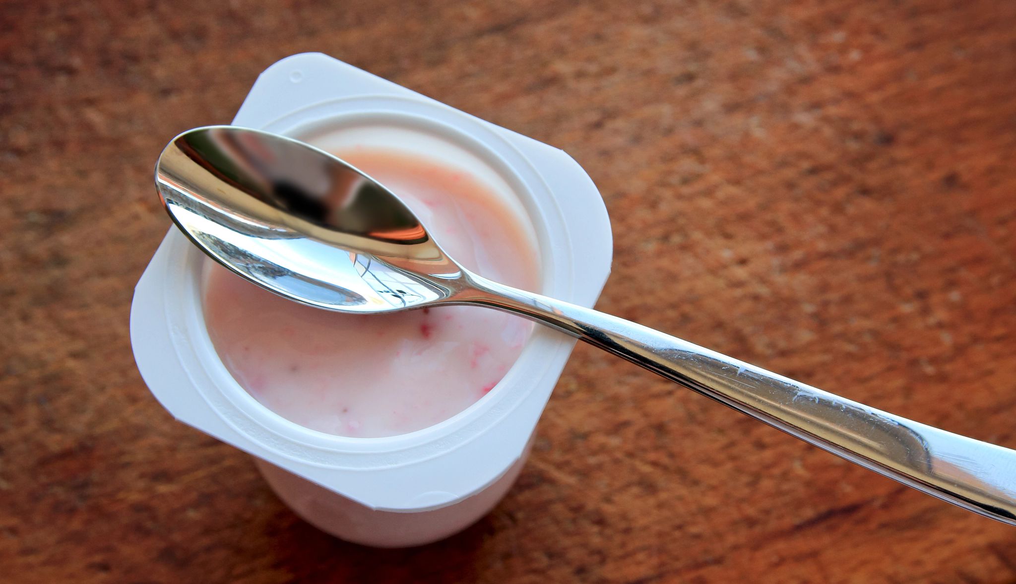 Strawberry pink yogurt in white plastic cup on a wooden rustic background with spoon on it.