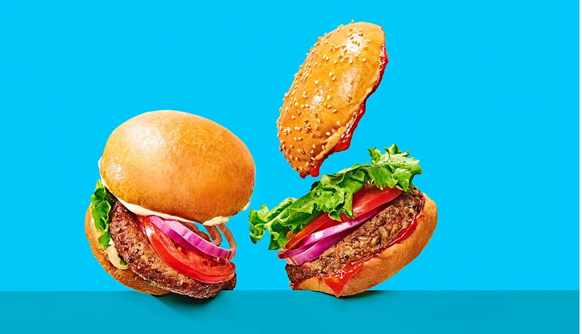 Veggie burger vs. Impossible Burger Two burgers on buns with lettuce, tomato, onions; one on the left has mayonnaise, one on the right has ketchup
