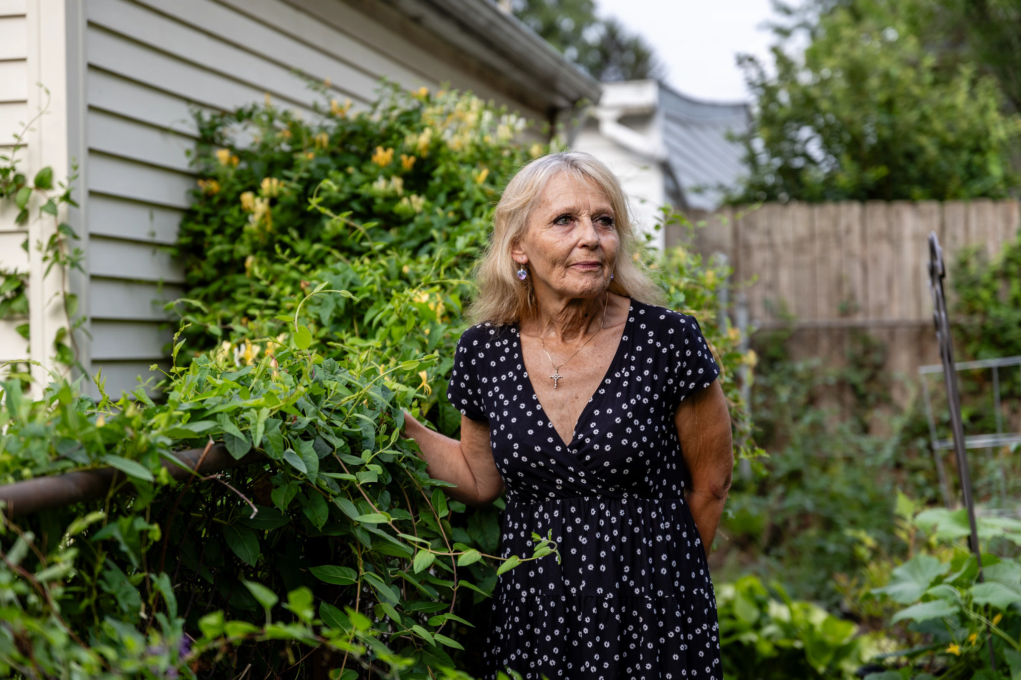 a woman in a black and white polka dot dress stands outside, surrounded by greenery