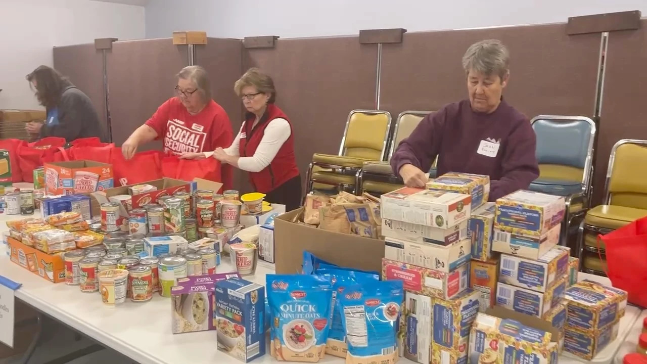 A group of volunteers in a community center sorting and packing non-perishable food items, like cans and boxes