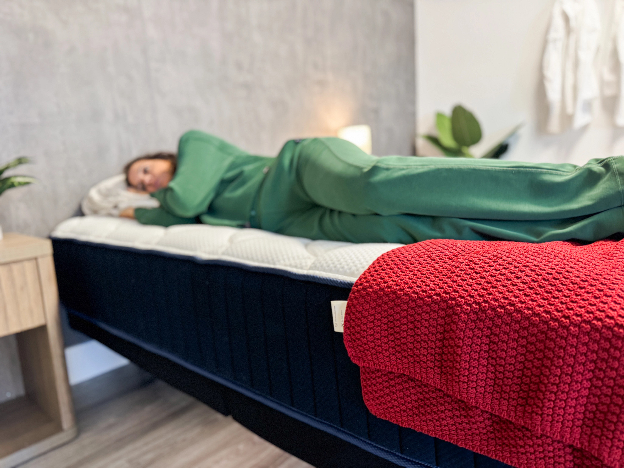 A woman lying on the edge of a mattress with a red blanket