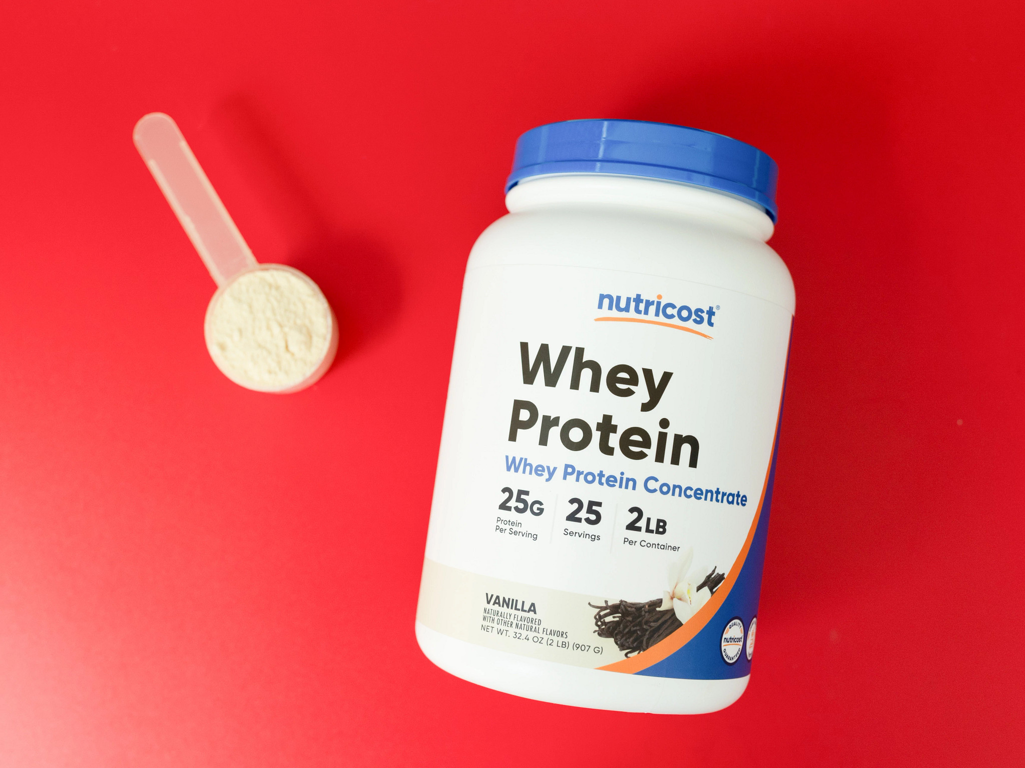 A container and scoop of Nutricost Whey Protein Concentrate Powder on a red background