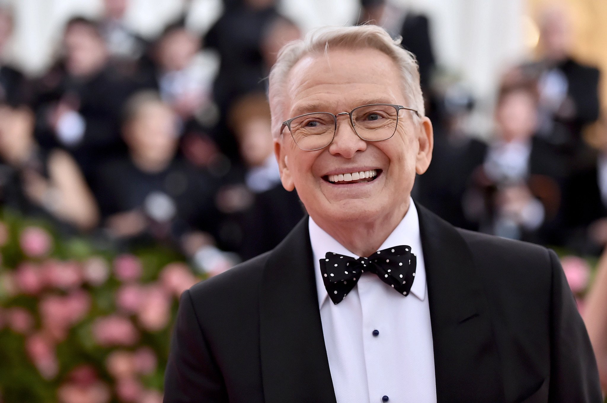bob mackie smiling in a tuxedo with a polka dot bowtie