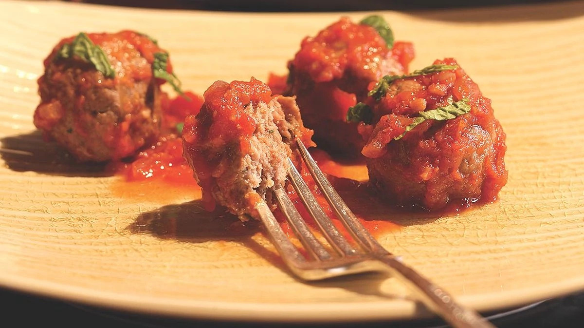 A close-up view of spicy lamb meatballs in tomato sauce on a plate