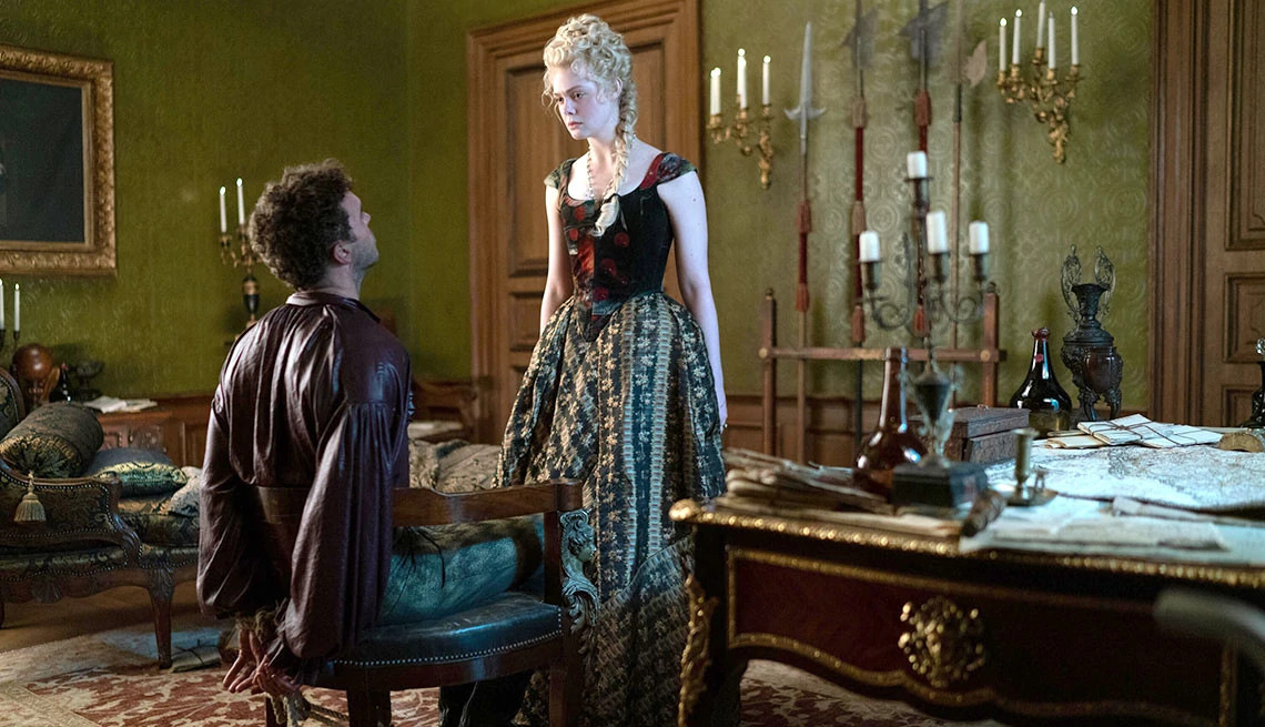 Nicholas Hoult sitting in a chair with Elle Fanning standing in front of him in The Great