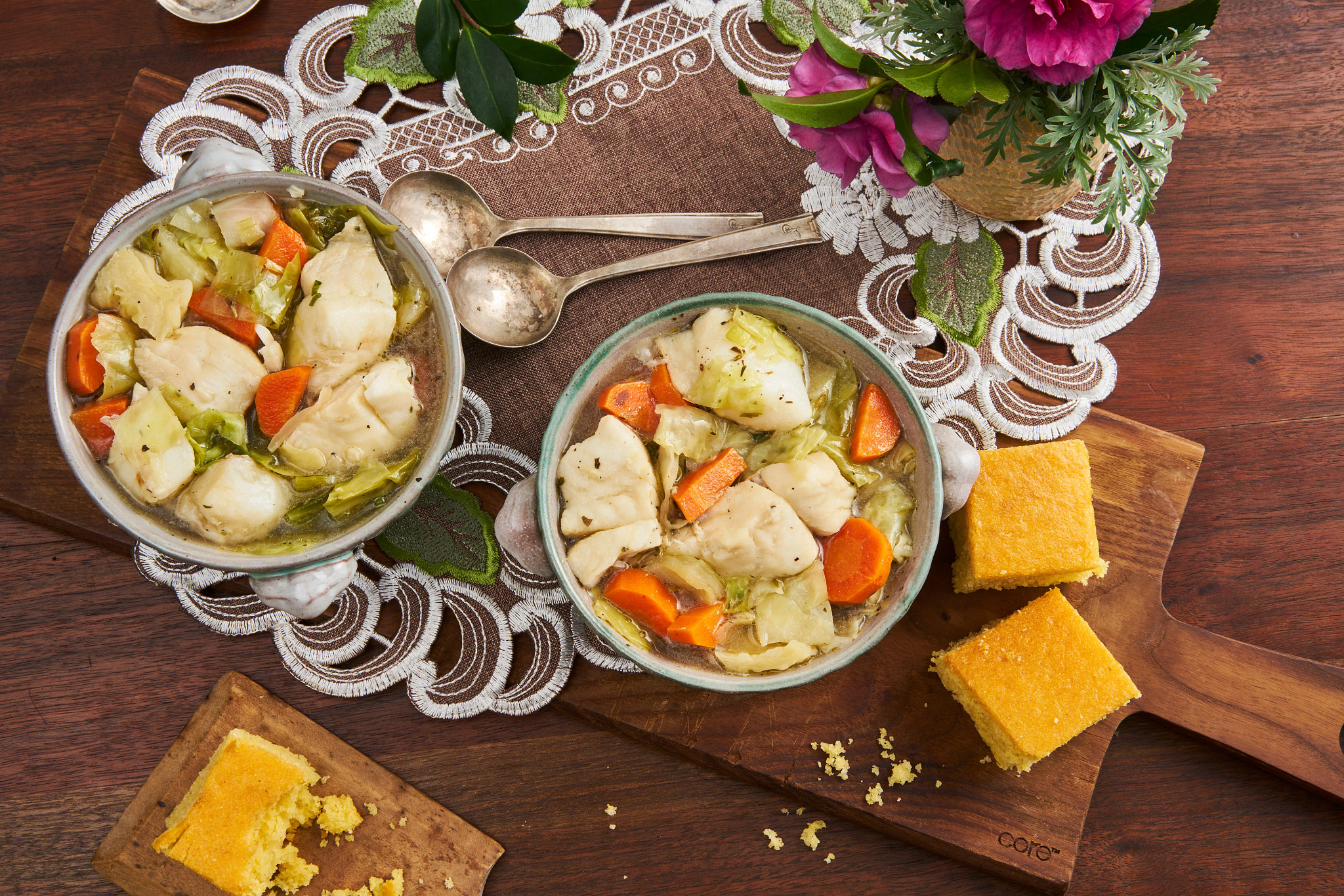 Two bowls of holiday soup with dumplings, carrots, and celery served with cornbread on a wooden table
