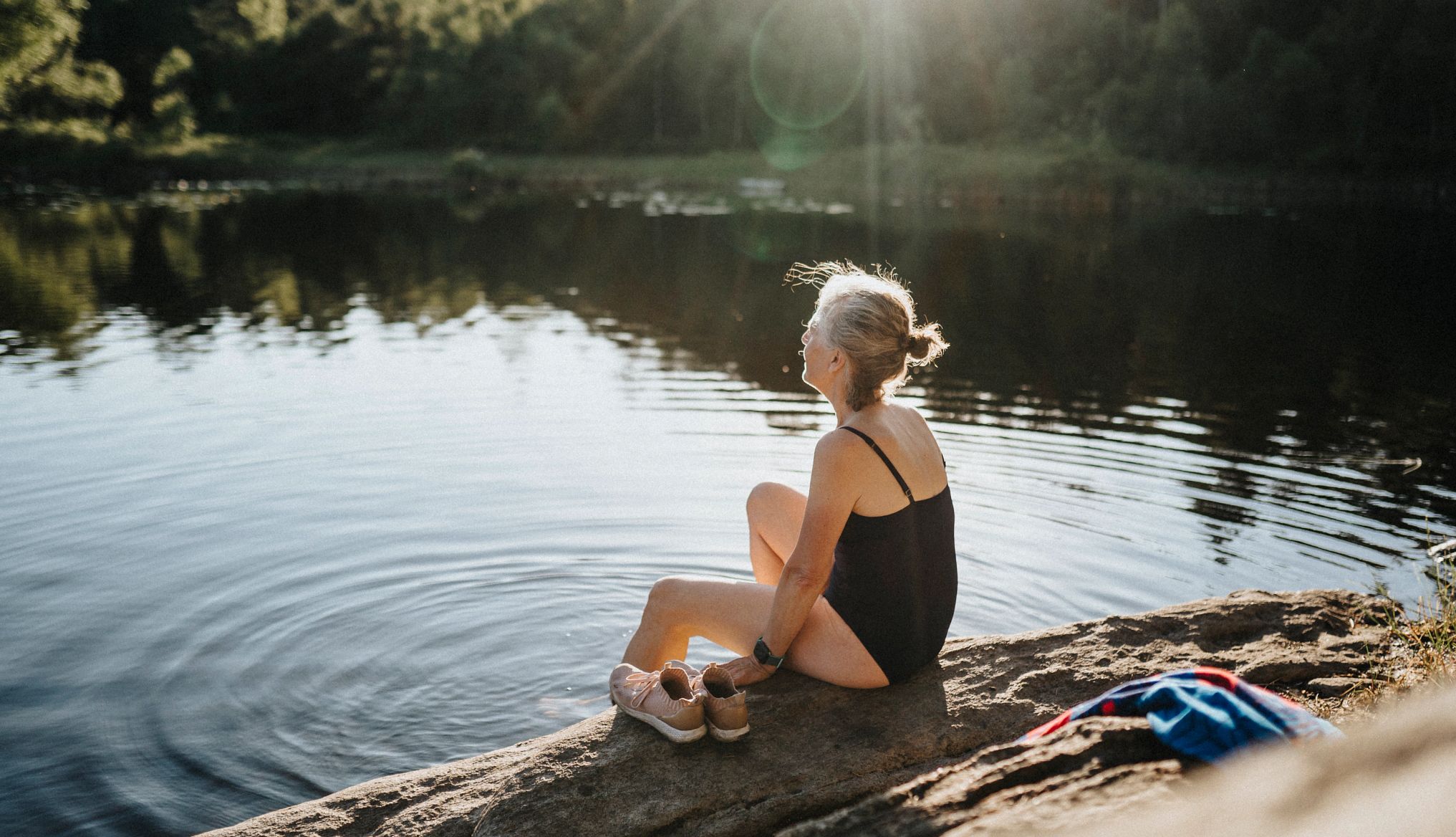 Woman at lake A woman in a swimsuit sitting on the ground with her feet in a lake