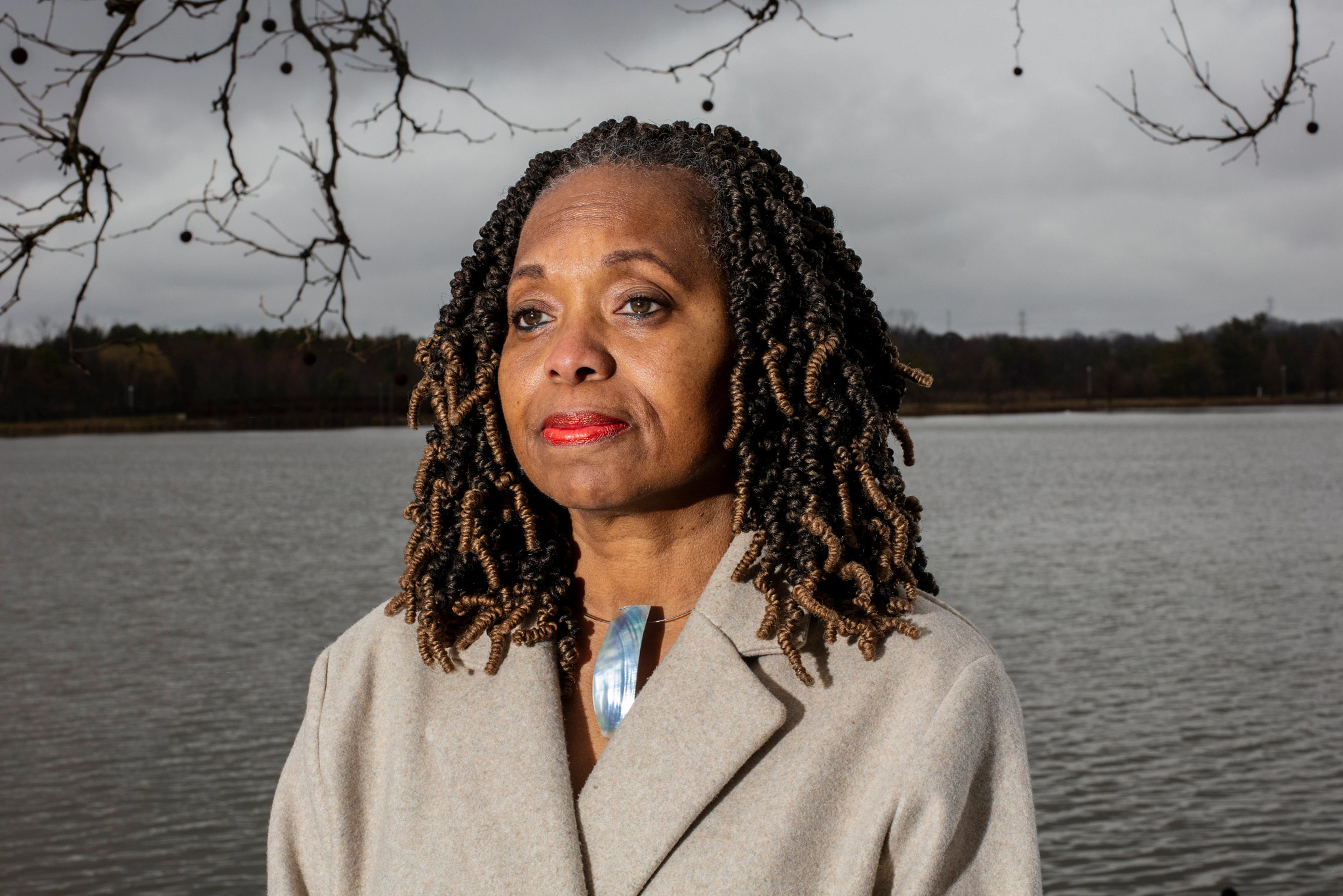 a woman stands in front of a lake, looking off screen