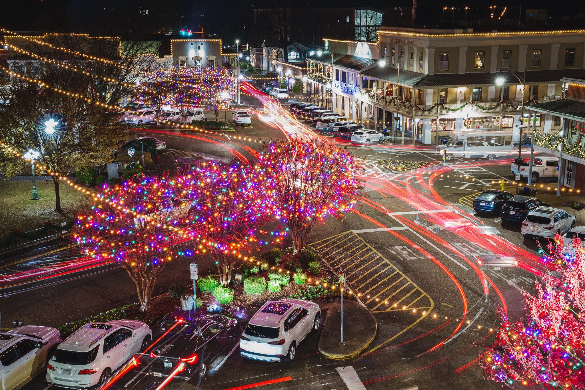 an overhead view of a street with motion blur light trails and trees with holiday lights