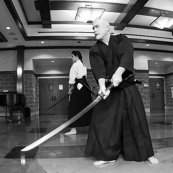 a black and white photo shows Kent Bradford practicing Nami ryu, a traditional Samurai martial art that combines swordsmanship and jiujitsu. 