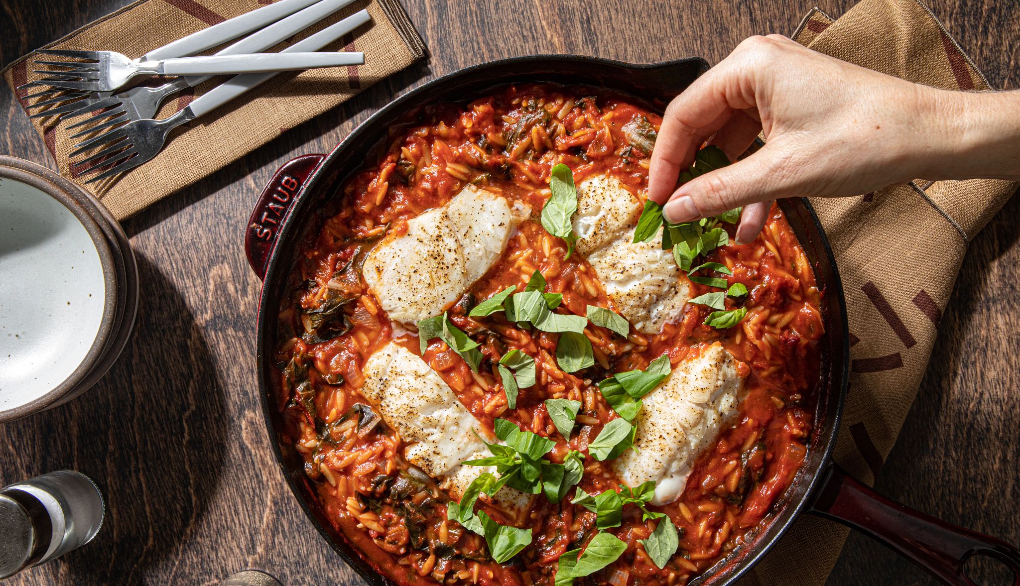 Cod & orzo arrabbiata Cod and orzo arrabbiata in dish with hand sprinkling green spices on it
