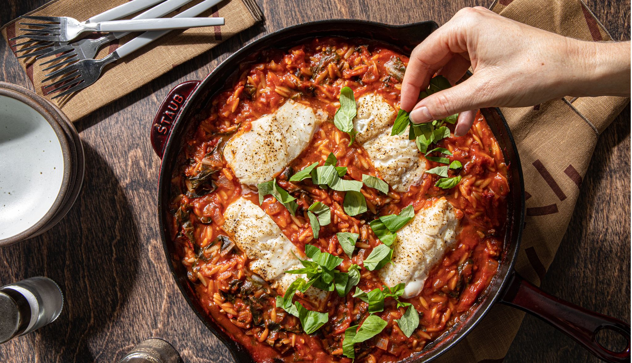 Cod & orzo arrabbiata Cod and orzo arrabbiata in dish with hand sprinkling green spices on it