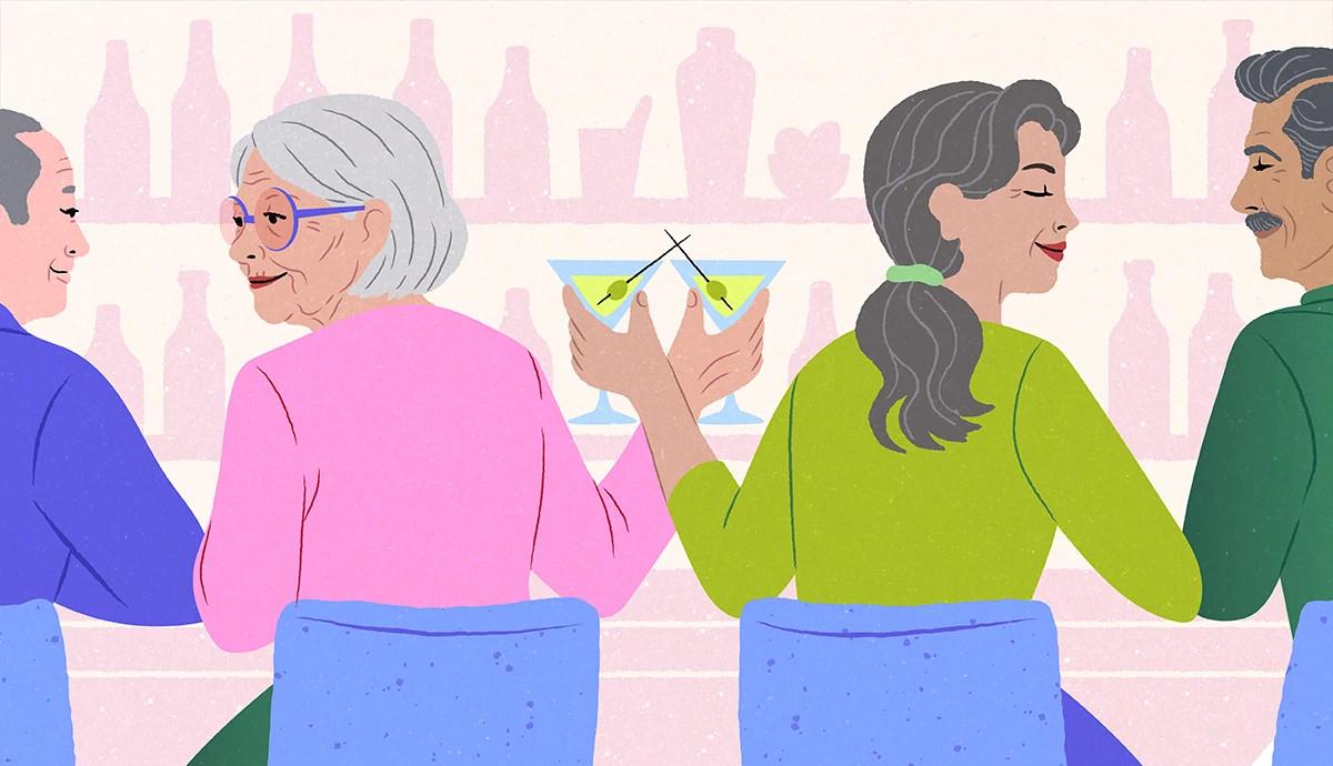 two women sit next to each other at a bar. they cheers their glasses while happily talking to the person on the other side of them