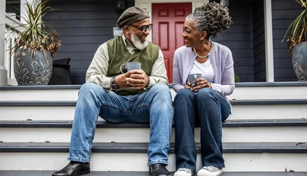 A man and woman chat over a cup of coffee while sitting on front porch steps.