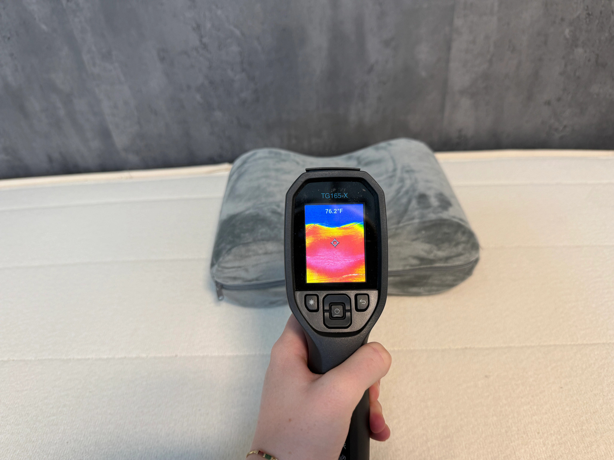 A hand holding a cooling gun aimed at a gray Sleep Number knee pillow