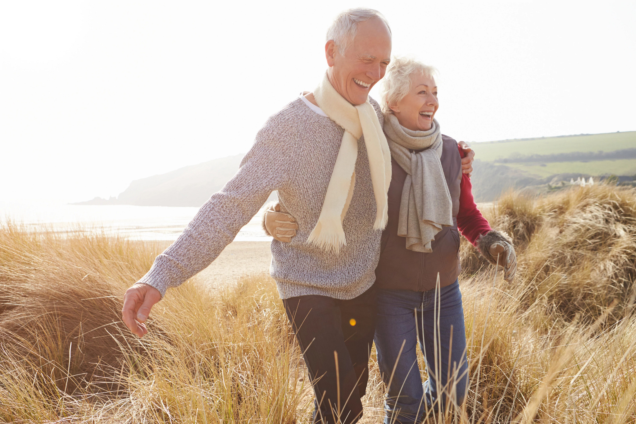 Senior Couple Walking Through Sand Dunes On Winter Beach