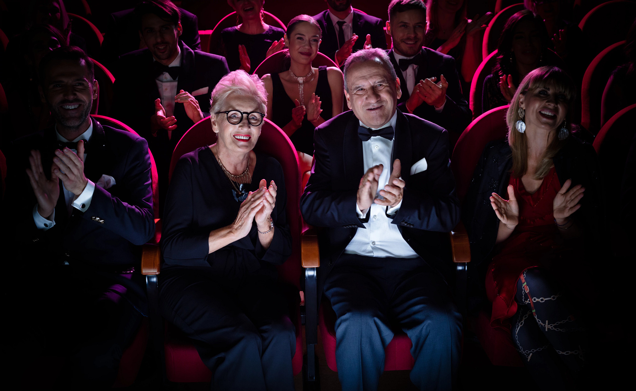 Happy senior couple applauding in theater. Elegant man and woman are watching in the audience.