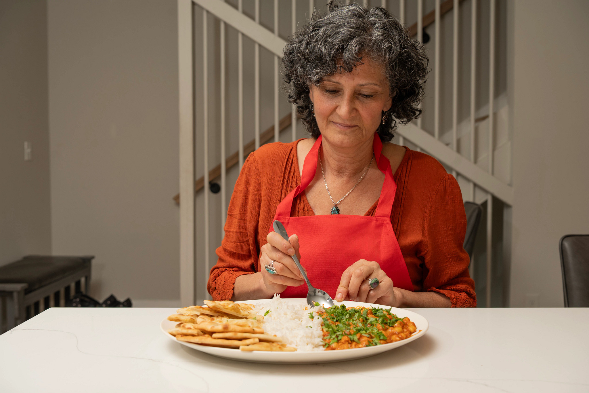 Woman smiles while preparing to eat her plate of chana masala with basmati rice and naan bread